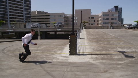 Businessman jumps over car in parking lot, slow motion