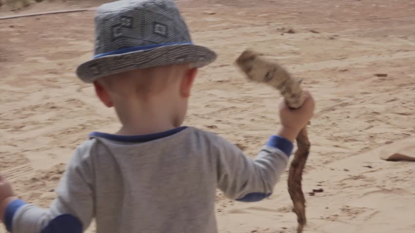 A boy playing in the desert with a stick