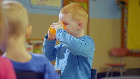 A cute little boy drinks from a cup during snack time