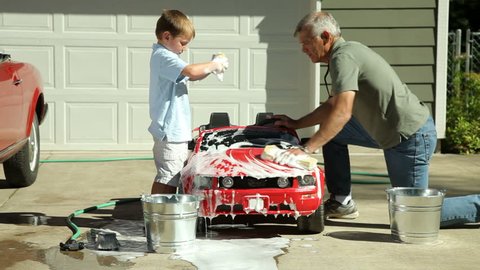 Grandfather and young boy washing car together 