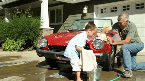 Grandfather and young boy washing car together 