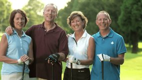 A group of older golfing buddies stand next to each other for a portrait on the course and smile at the camera