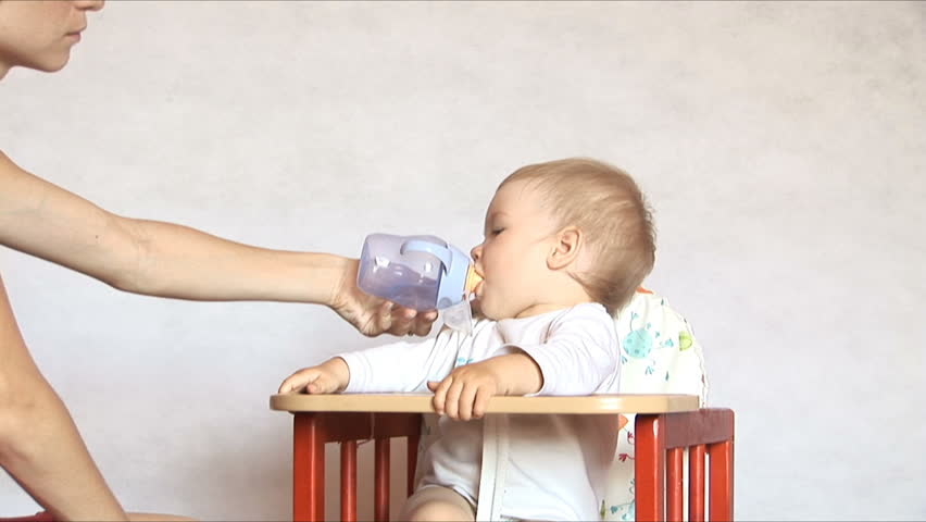 Baby sits at a children's little table. Mum gives to drink water of the child.