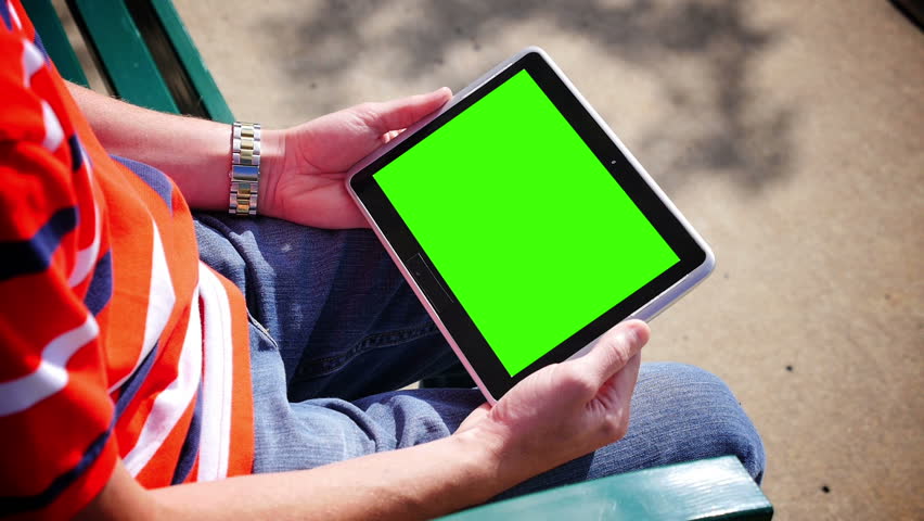 A man on a park bench holds a blank tablet PC in landscape orientation with a