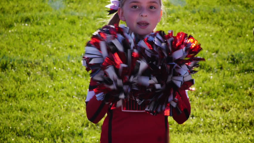 A young girl cheerleader on the sidelines with her pompoms.