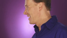 A man turns to the camera and smiles and laughs on purple