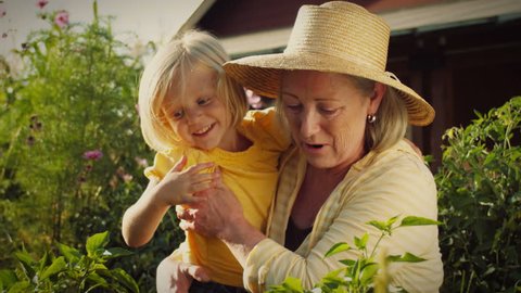 A little blonde girl runs to her grandmother's arms in a garden.