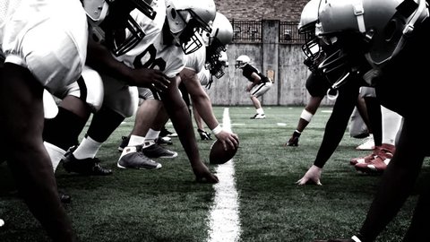 The defensive and offensive lines of two football teams meet at the line of scrimmage. High contrast, with camera flashes and time remap.