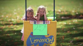 Two little girls look around for customers at their lemonade stand. medium shot.