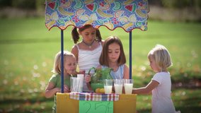 Little girls work together to pour lemonade. wide shot.