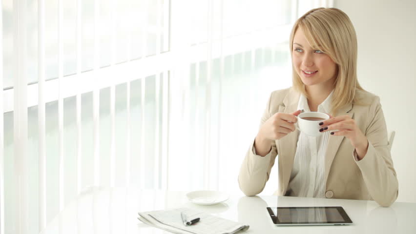 Charming young woman sitting at table drinking coffee and smiling at camera