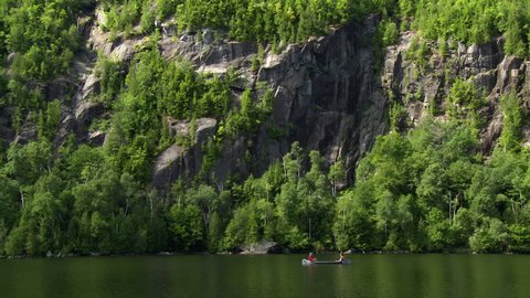Two men rowing in a canoe on a beautiful rural lake under rocky cliffs