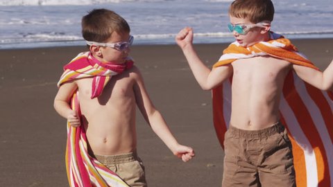 Young boys at beach flexing muscles with superhero costume