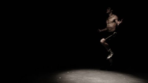 A fighter does some jump rope exercises in a dark room under a light