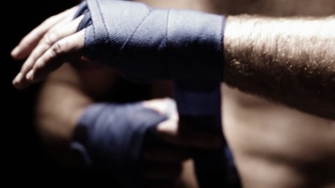 Mixed martial arts athlete wraps his hand with blue cloth. Close up shot.