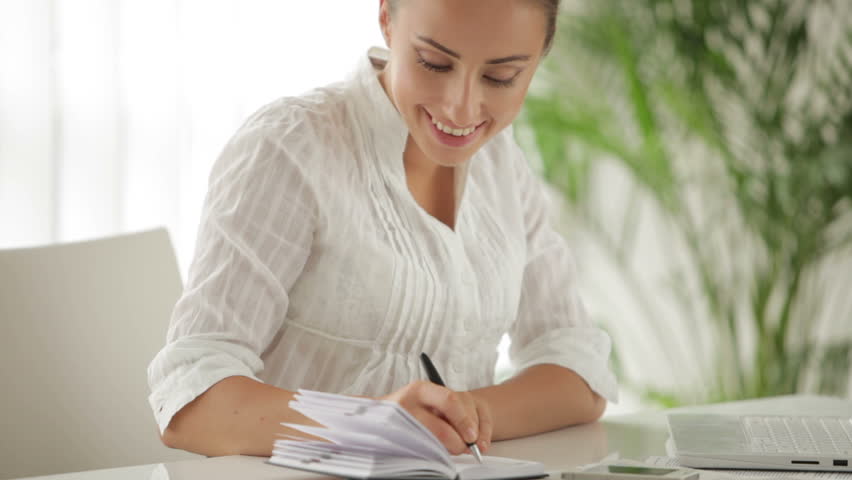 Businesswoman sitting at table using laptop and writing in notebook