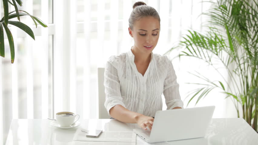 Businesswoman sitting at table using laptop and cellphone
