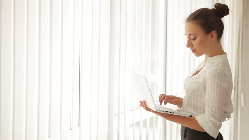 Charming business woman standing in front of window and using netbook