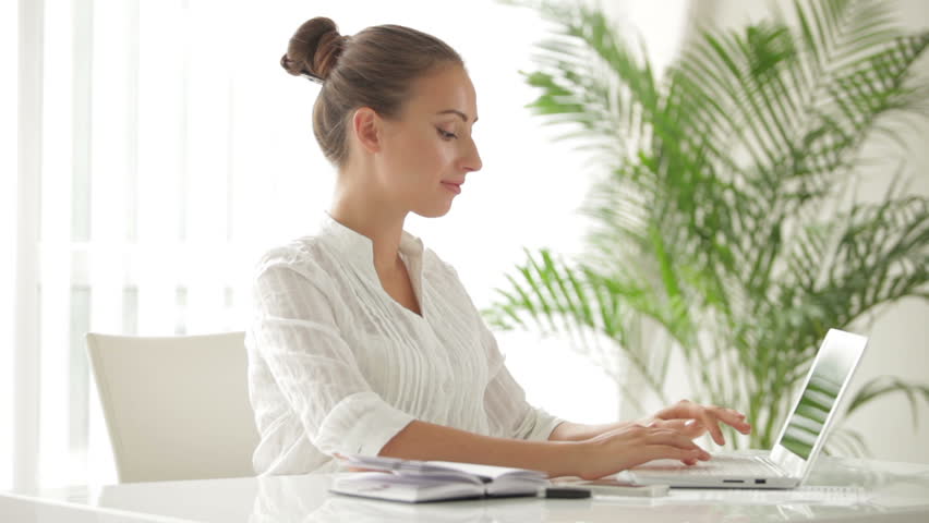 Charming businesswoman sitting at table using laptop and smiling