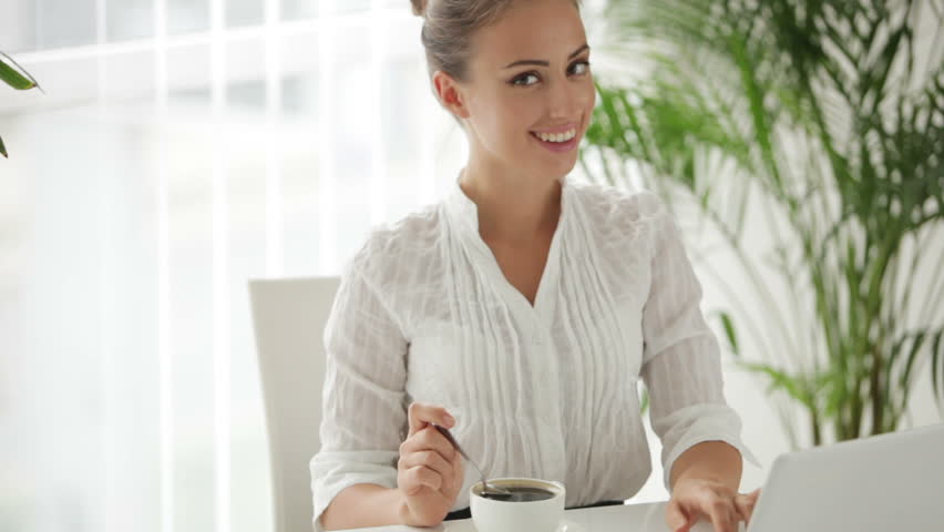 Businesswoman sitting at table with cup of cofee and using laptop with smile