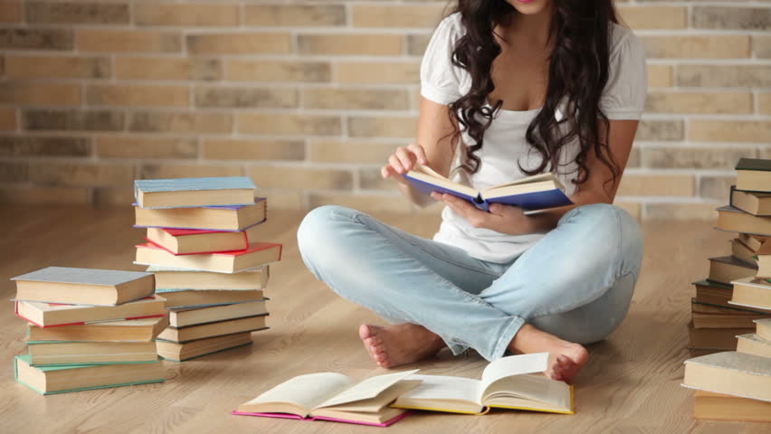 Charming brunette girl sitting on floor reading book and smiling at camera