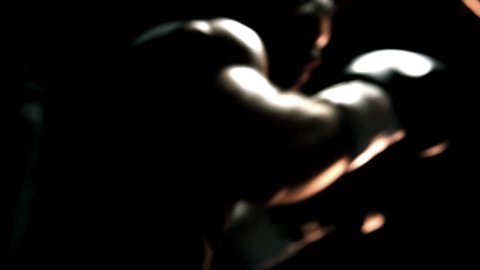 Muscular athlete practices boxing on a punching bag. Close up shot.