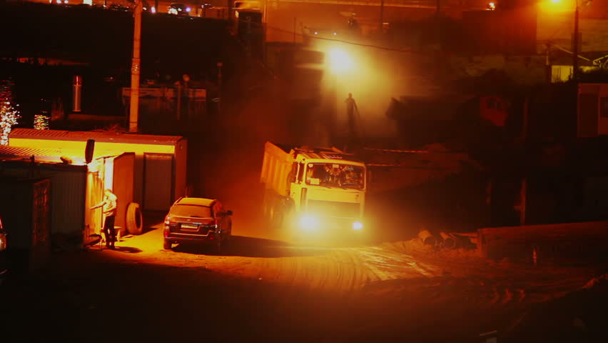 Construction site at night, trucks lorries drive in out, yellow