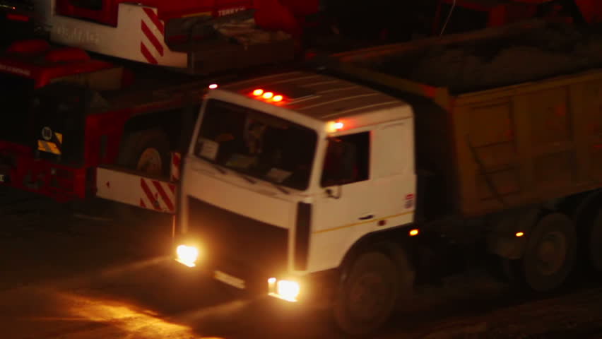 Construction yard trucks drive, working machines, night site