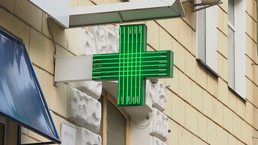 Pharmacy, drug store green neon cross lighted at daytime, city