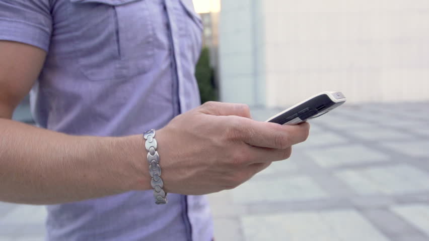 Slow Motion Shot Of A Male Hand Dialing The Mobile Phone While Walking 
