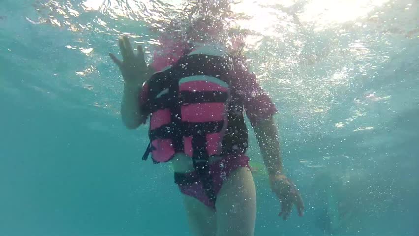 A girl in a life jacket at the swimming pool underwater shot