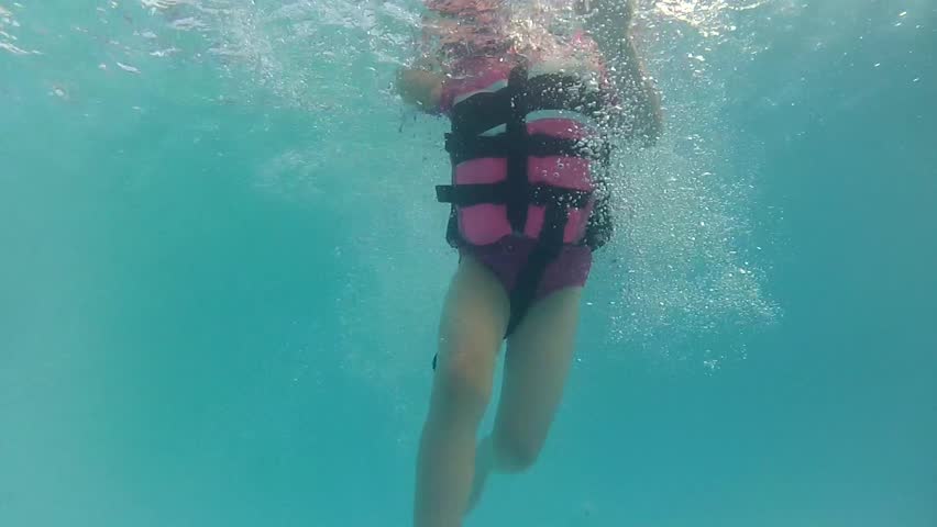 A girl jumps into a pool with a life jacket underwater shot