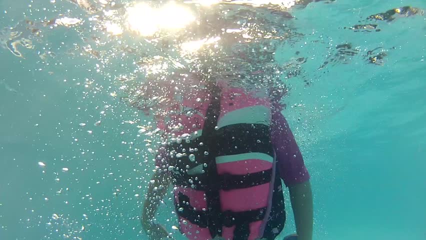 A girl with a life jacket and swim goggles in the swimming pool underwater shot