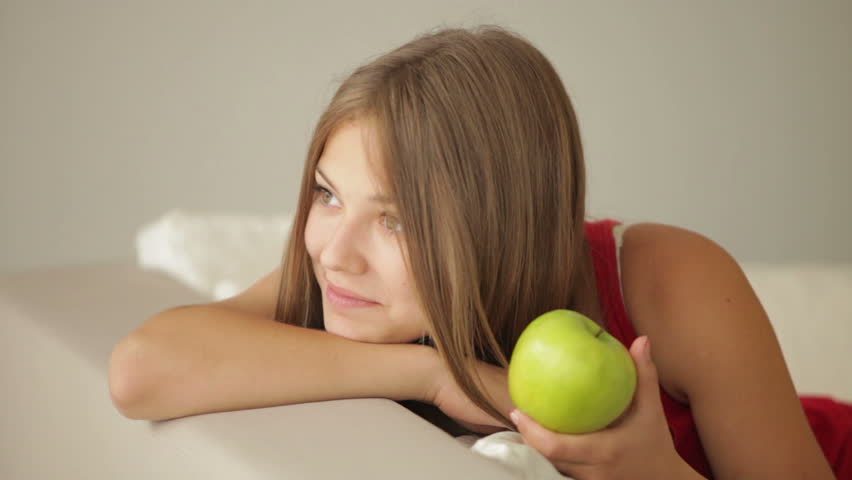 Pretty girl relaxing on sofa eating apple and smiling