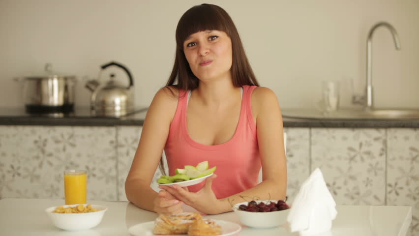 Cute girl sitting at kitchen table and eating sliced fruit