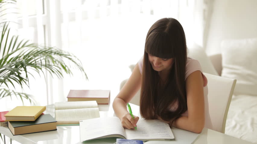 Cute girl sitting at table studying and writing in notebook