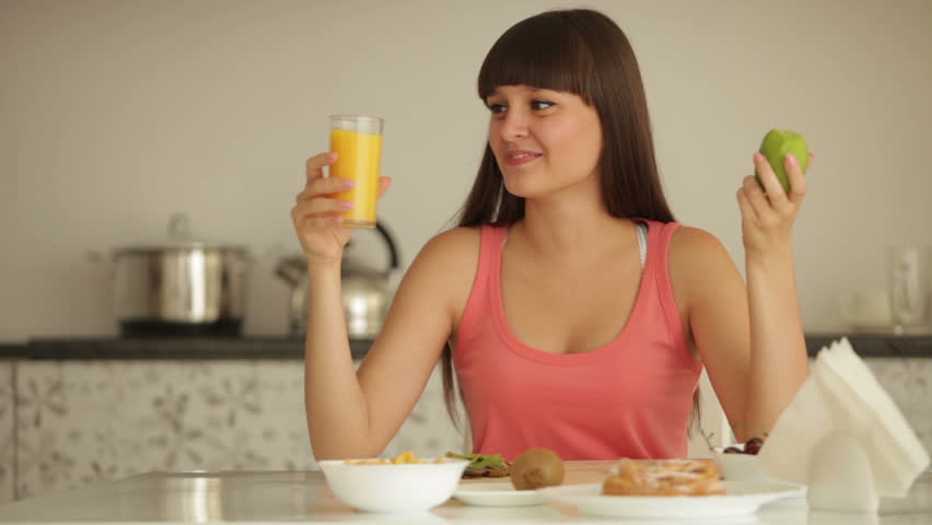 Cute girl sitting at kitchen table eating kiwi and drinking juice