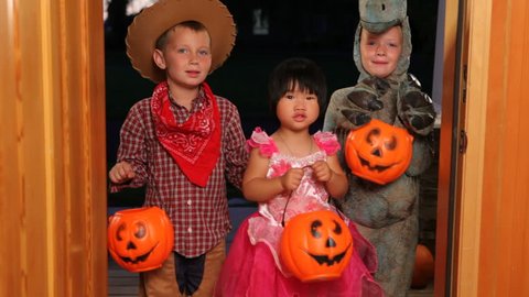 Three children in Halloween costumes trick or treating Stock Video