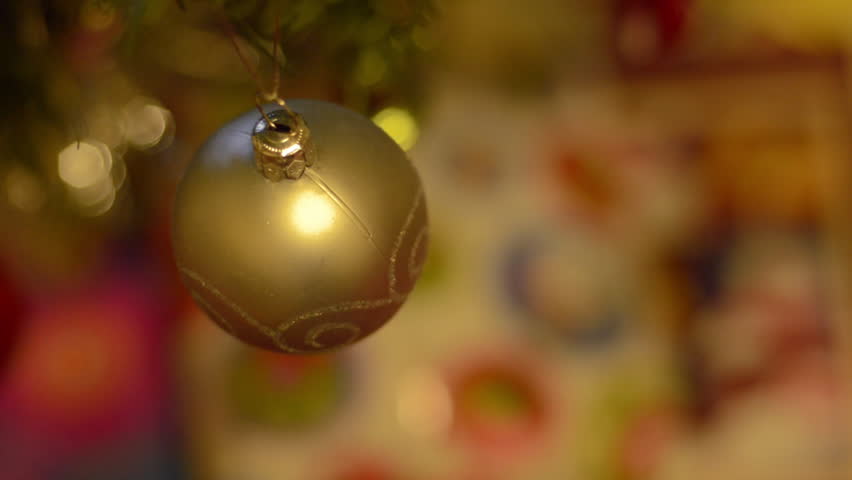 A yellow bauble hanging on a Christmas tree, focus racking to a wrapped present
