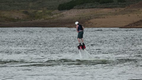 Young Man learning how to Fly Board mountain lake. Flyboard is a aerial machine for a personal watercraft which allows propulsion underwater and in the air allowing a person to fly like Iron Man.
