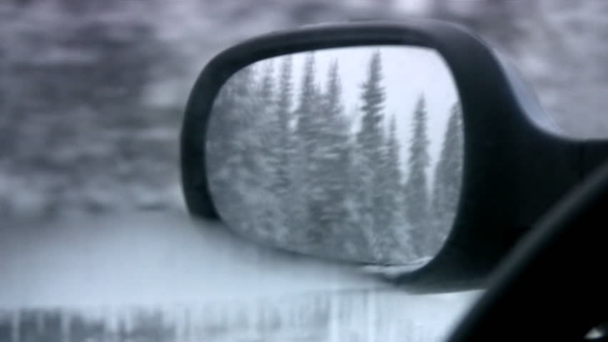 Kind in the left mirror of a back kind of car on a wood covered with snow and