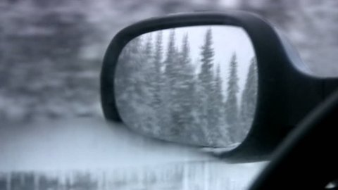 Kind in the left mirror of a back kind of car on a wood covered with snow and lake, covered by ice during movement on a winter road. Twilight. Finland. North