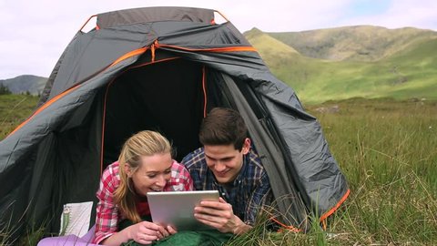Happy couple using a digital tablet lying in their tent in the countryside