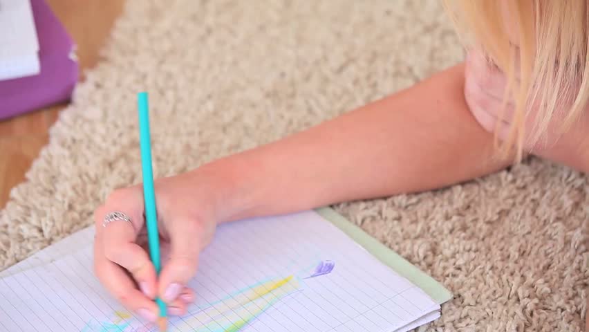 Attractive young blonde making colourful drawing while lying in her living room