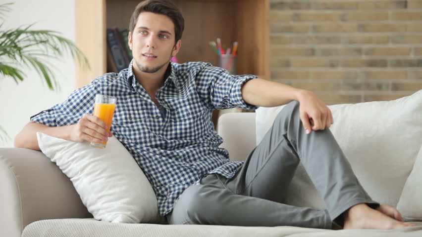 Cheerful guy relaxing on sofa holding glass of juice and smiling