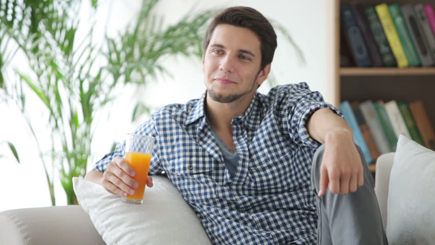 Cheerful guy sitting on sofa drinking juice and smiling