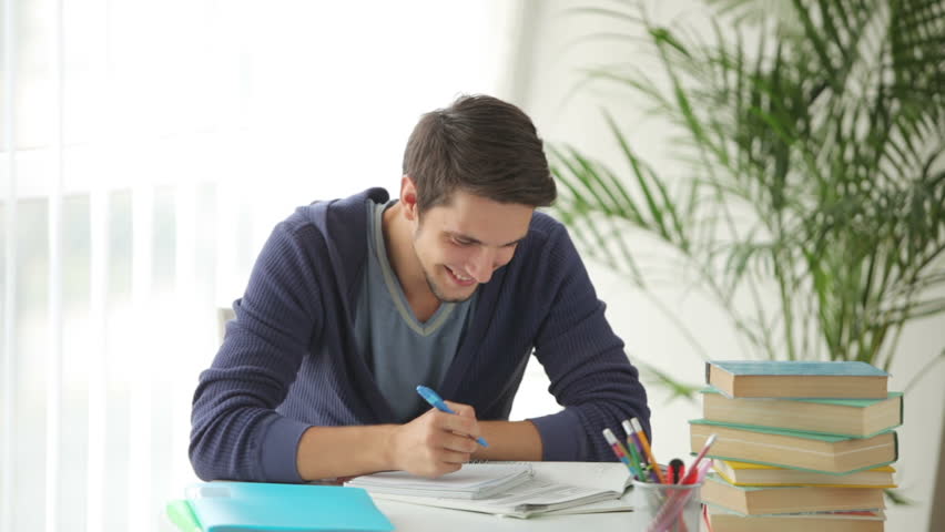 Charming guy sitting at table with books and studying