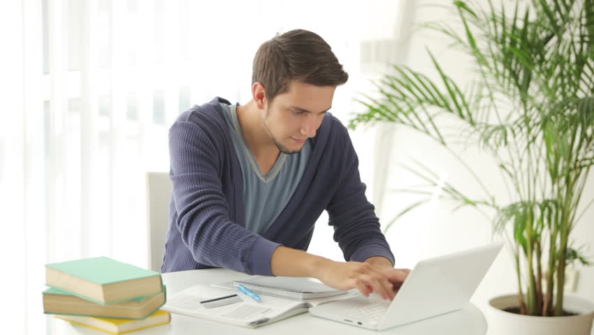 Cheerful guy sitting at table with laptop and credit card