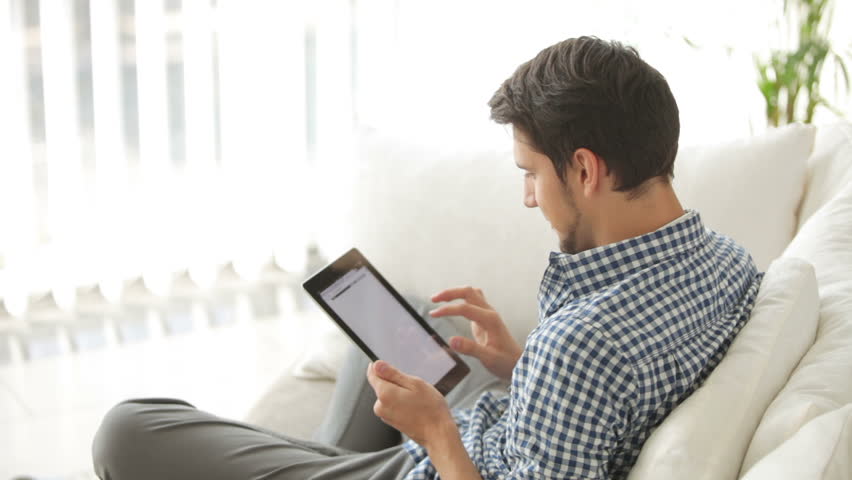 Charming guy sitting on sofa and using touchpad