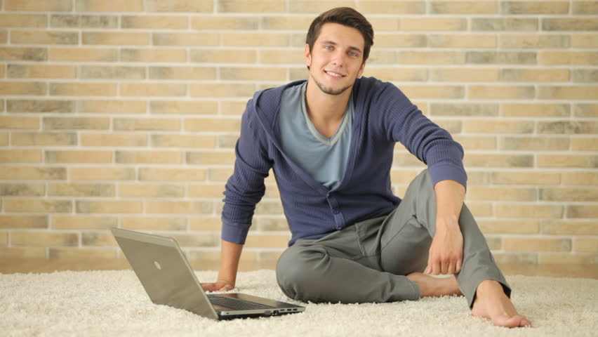 Cheerful guy stting on floor and using laptop